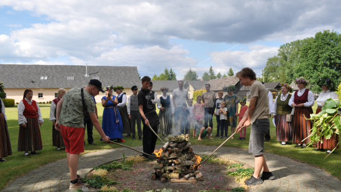 Līgo ugunskura iekurināšana. Līgotāji nostājušies aplī, muzeja pagalmā ap ugunskura vietu
