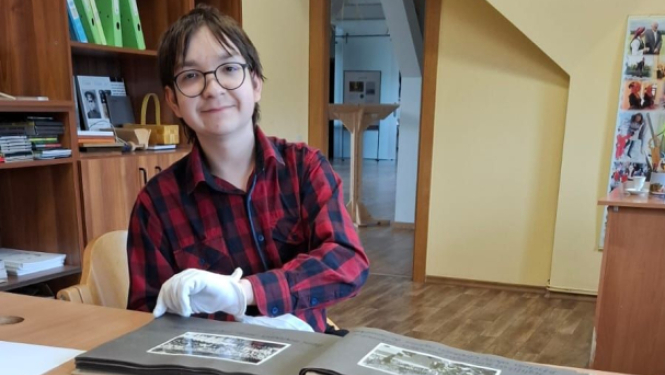 10. klases skolnieks sēž pie galda un iepazīstas ar muzeja darba ikdienu