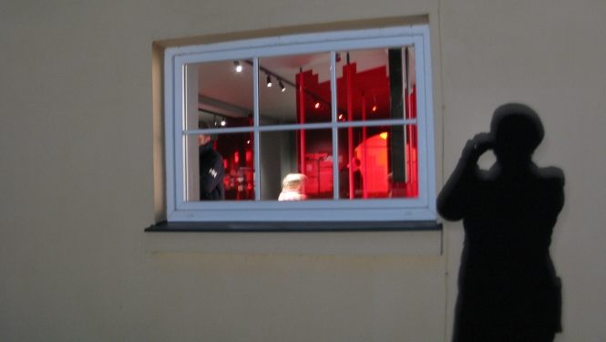 Ēna uz muzeja sienas, kura fotogrāfē ekspozīciju caur muzeja logu