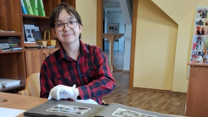 10. klases skolnieks sēž pie galda un iepazīstas ar muzeja darba ikdienu