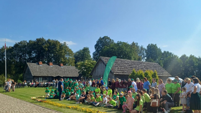 Kārlim Ulmanim veltītā atceres pasākuma dalībnieki muzeja pagalmā pie krāšņas ziedu lentes