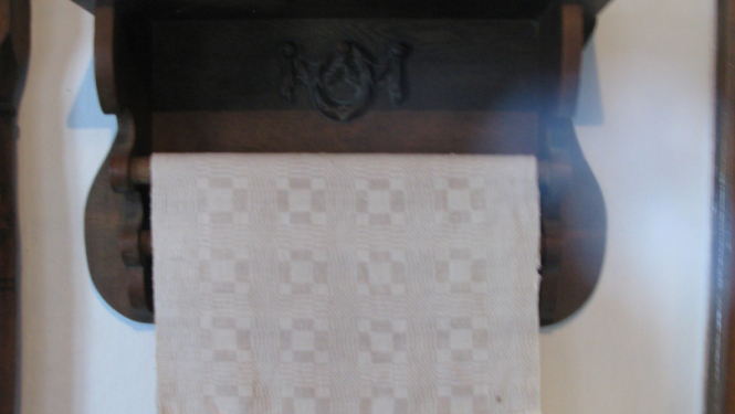 Lina dvielis uz koka pakaramā pie gaišas sienas, muzeja telpās