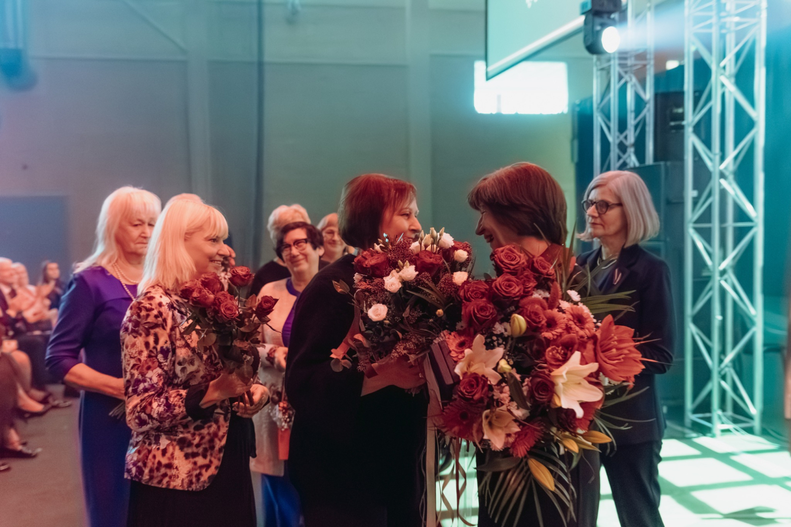 Cilvēku pūlis ar ziediem sveic sievieti apbalvošanas ceremonijas laikā