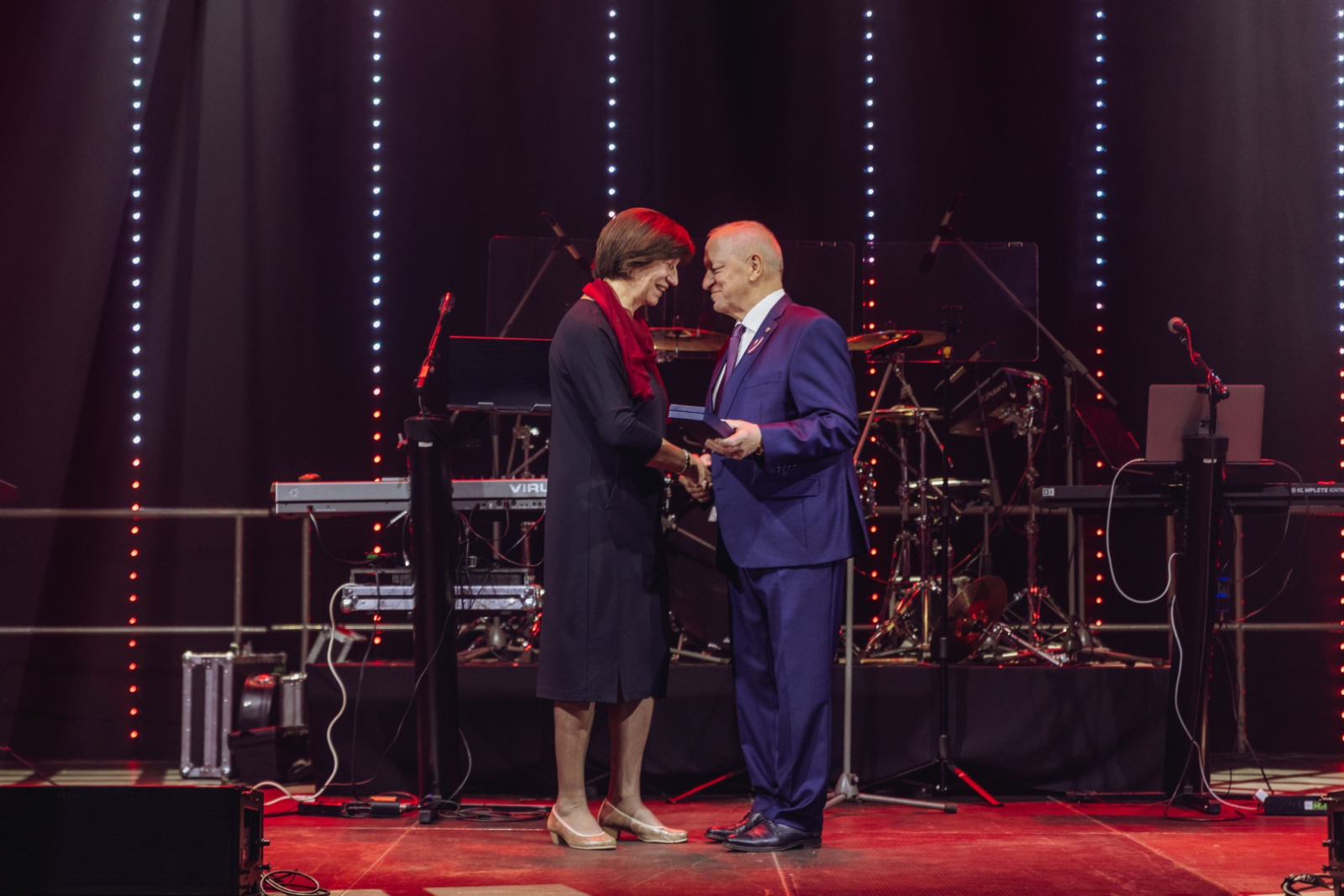 Sieviete un vīrietis viens otram paspiež roku. Vīrietis pasniedz Dobeles novada pašvaldības apbalvojumu