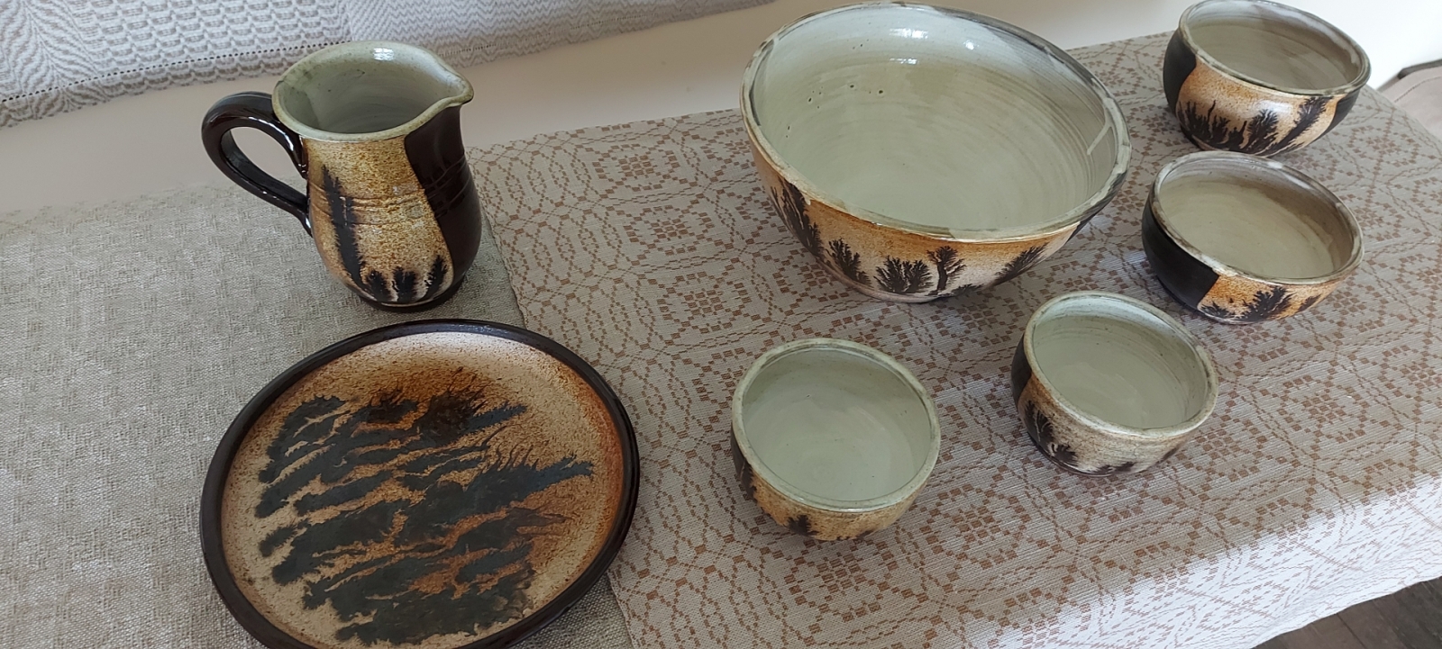 Uz galda linu dvielis, uz kura dažādi keramikas trauki