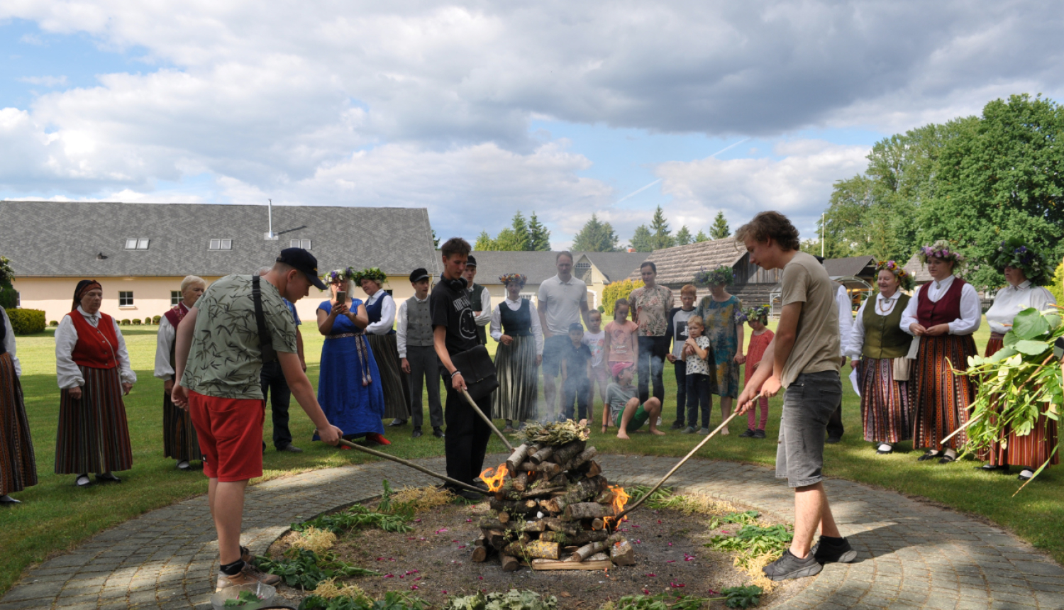 Līgo ugunskura iekurināšana. Līgotāji nostājušies aplī, muzeja pagalmā ap ugunskura vietu