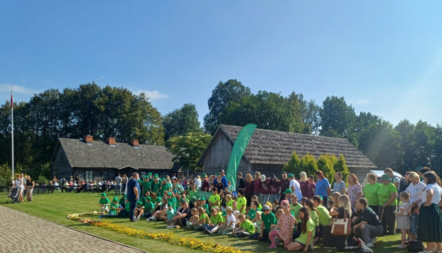 Kārlim Ulmanim veltītā atceres pasākuma dalībnieki muzeja pagalmā pie krāšņas ziedu lentes