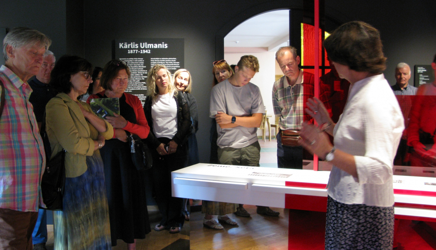 Pūlis muzeja ekspozīcijā klausās gidu