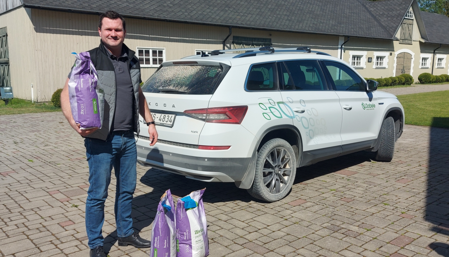 Muzeja pagalmā vīrietis stāv pie automašīnas ar zivju barības paku rokā