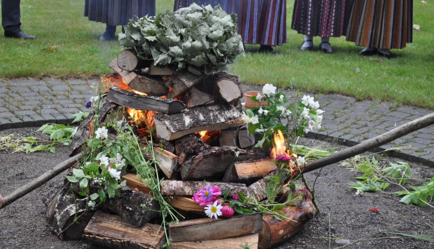 Līgo vakara zālēm pušķots ugunskurs. Notiek ugunskura aizdedzināšana.